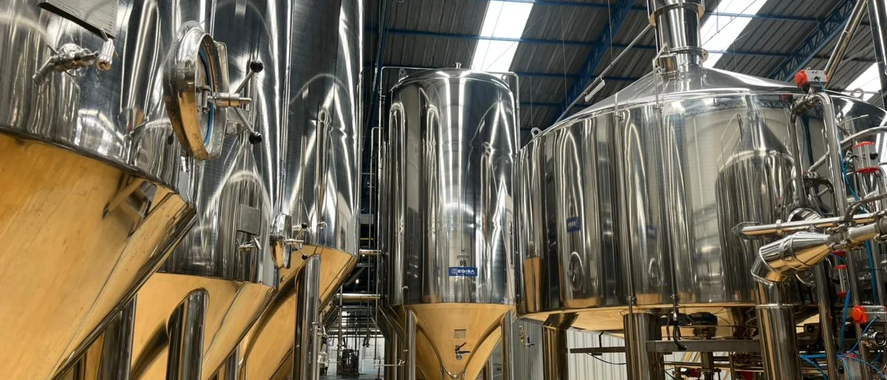 Tanques de fermentação da Ravache vistos de perto, com a estrutura do galpão ao fundo